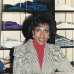 Iris poses in front of shelves of merchandise in an minimalist store setting