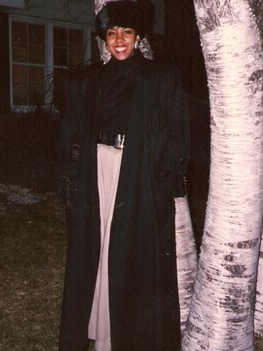 Ebonnie Rowe in black coat standing in front of trees