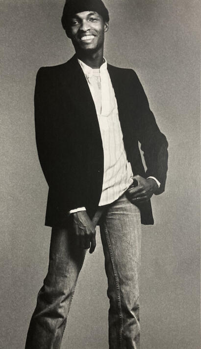 Man wearing a blazer over a button-up shirt with jeans, smiling confidently.