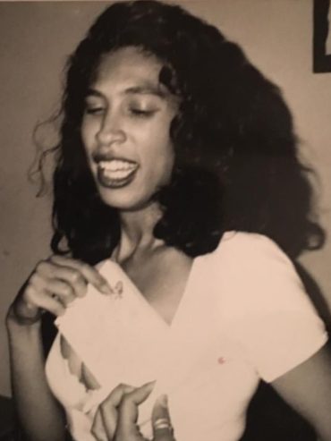 A youthful Sharmain captured in a candid moment, with dark, curly hair and a white top.