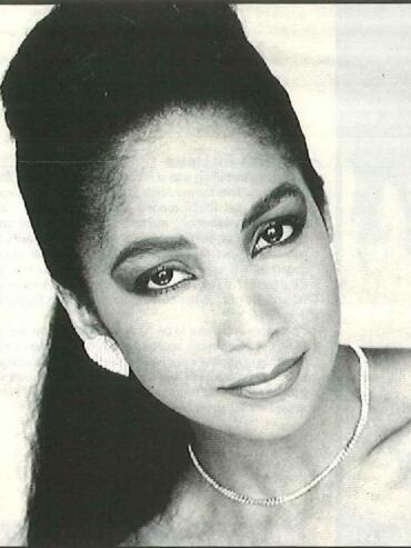 Black-and-white portrait of a woman with styled hair and elegant jewelry.