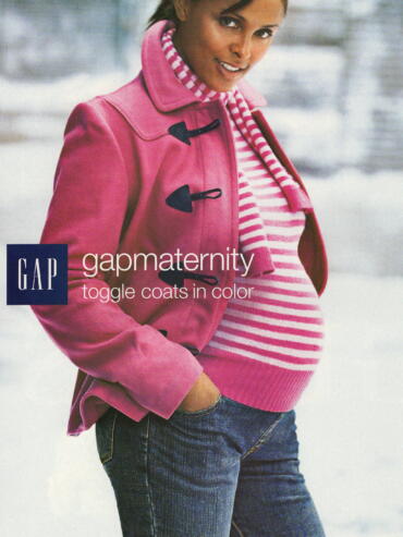 A pregnant woman in a pink toggle coat, striped sweater, and jeans outdoors.