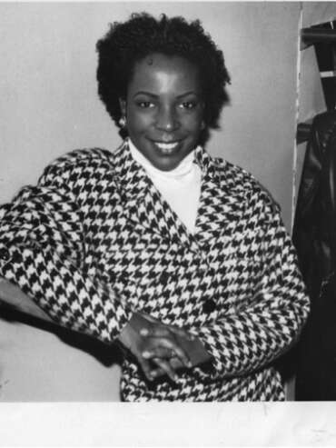 Black-and-white photo of a smiling woman in a houndstooth blazer inside a fashion boutique.