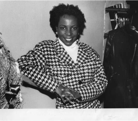 Black-and-white photo of a smiling woman in a houndstooth blazer inside a fashion boutique.
