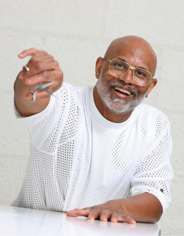 An older man with glasses, a beard, and a white perforated shirt, smiling and holding out a ring.