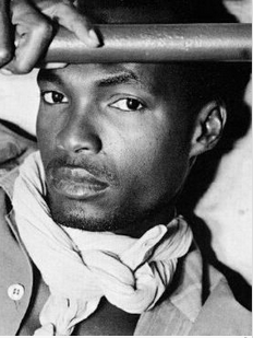 Black and white portrait of a man with a scarf around his neck, gazing confidently at the camera.