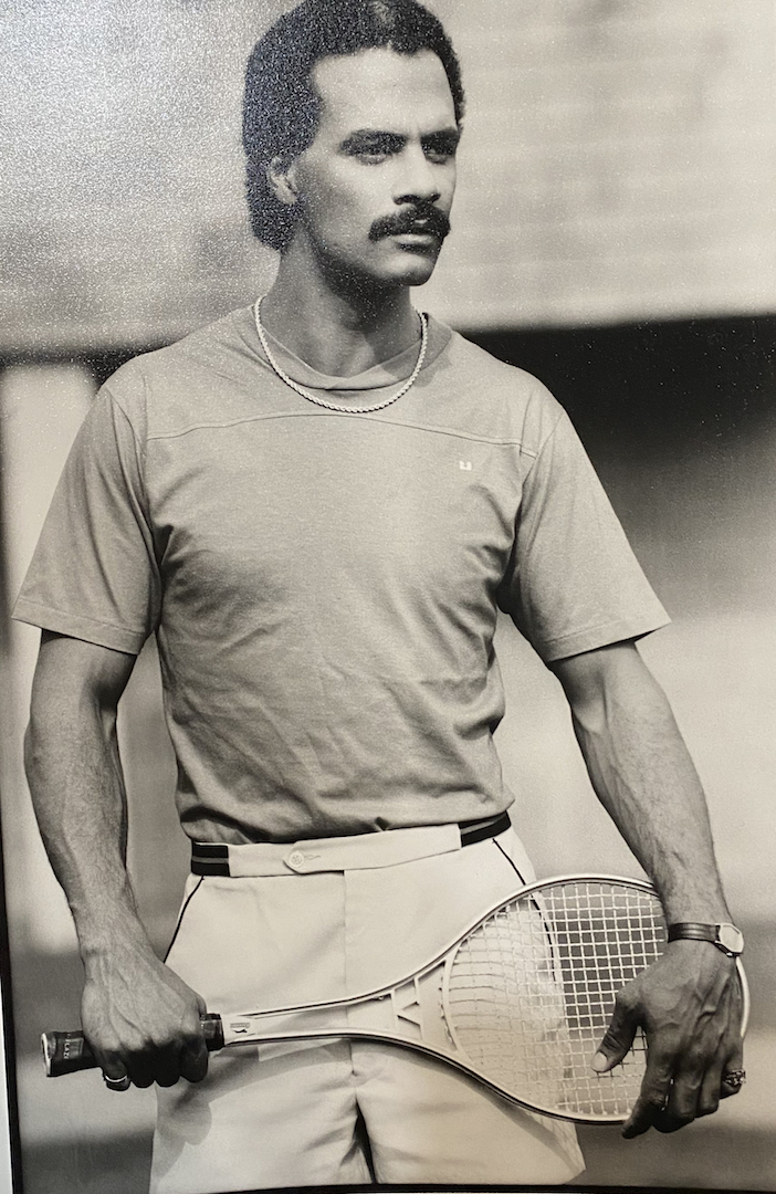 Male tennis player in vintage sportswear, holding a racket, on a tennis court.