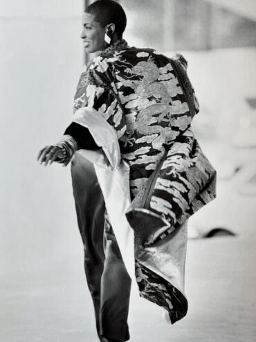 Woman in patterned kimono with a large shoulder bag, smiling and walking confidently.