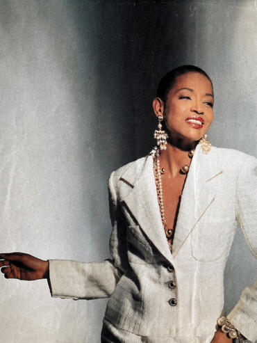 Elegant woman in a white textured blazer with statement jewelry, smiling confidently.