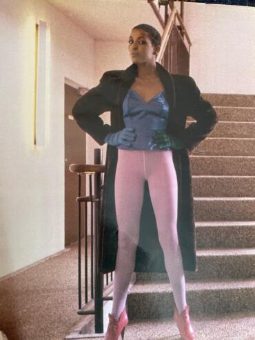Fashion-forward woman in a long coat, colorful tights, and high heels standing on staircase.