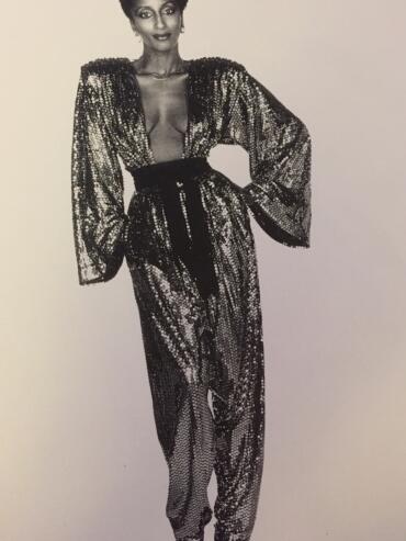 Black and white photograph of a woman in a sequined, deep V-neck jumpsuit with wide sleeves and high-waisted pants.