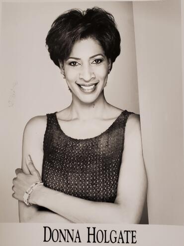 Black-and-white portrait of a woman with short, voluminous hair, wearing a sleeveless textured dress and jewelry.