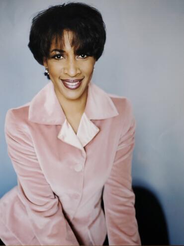 Professional portrait of a woman with short black hair, wearing a pink suit and white shirt.