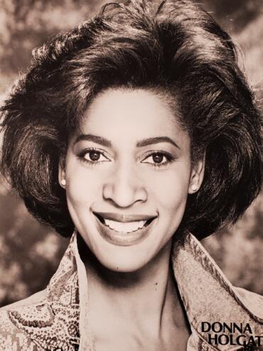 Black-and-white portrait of Donna Holgate with voluminous hairstyle, smiling.