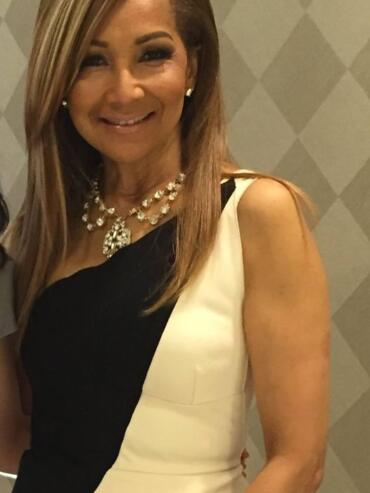 Woman wearing a black and white dress with pearl jewelry, smiling at a formal event.