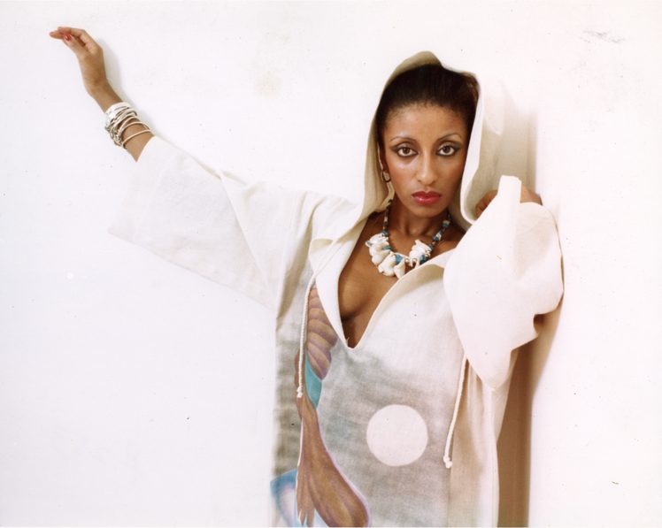 Stylish woman in a white embossed hoodie with colorful patterns, accessorized with jewelry.