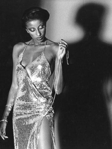 Elegant woman in a shimmering, slit dress holding a string, black and white photo.