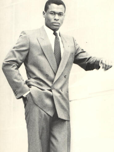 A man in a pinstripe suit poses confidently against a plain background, exuding classic style.