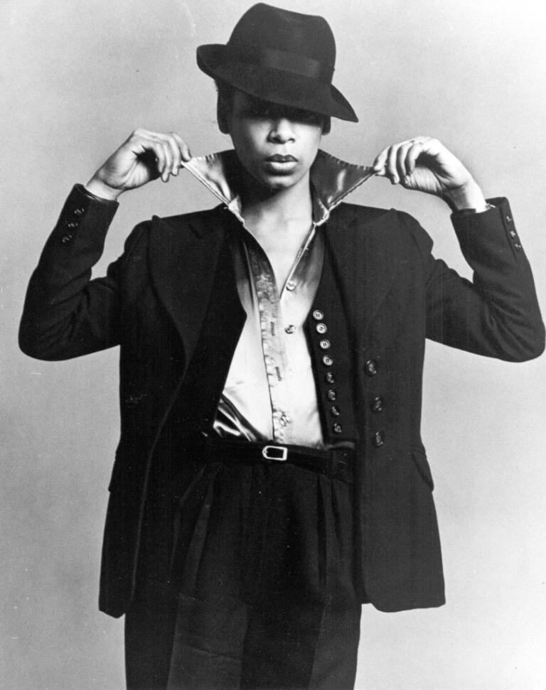 Black and white fashion photograph of a woman in an oversized blazer, silk shirt, and a wide-brim hat.