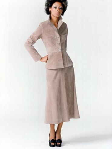 Woman in a taupe suit with a matching skirt, classic style, against a plain backdrop.