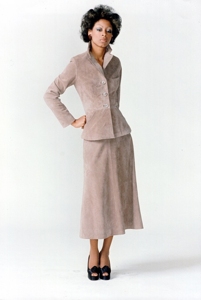 Woman in a taupe suit with a matching skirt, classic style, against a plain backdrop.