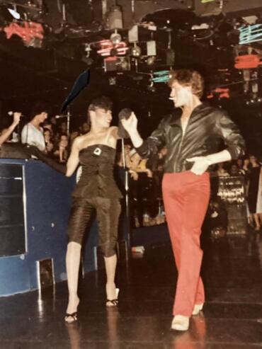 Two women dance and smile on a lively, illuminated dance floor at a party.