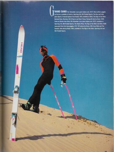 Female skier in colorful winter gear on sandy slope under a clear blue sky.