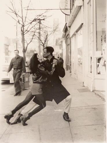 Couple dancing passionately on city sidewalk in an artistic black-and-white photo.