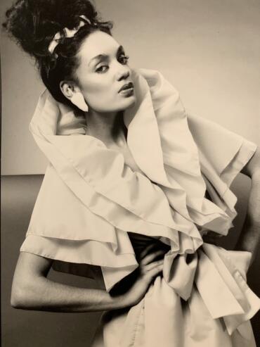 Black and white portrait of a woman in high fashion with voluminous hair and statement clothing.