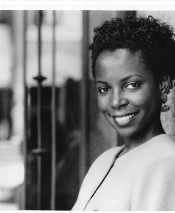 Black and white portrait of a smiling woman with short, curly hair, wearing earrings and a light-colored top.