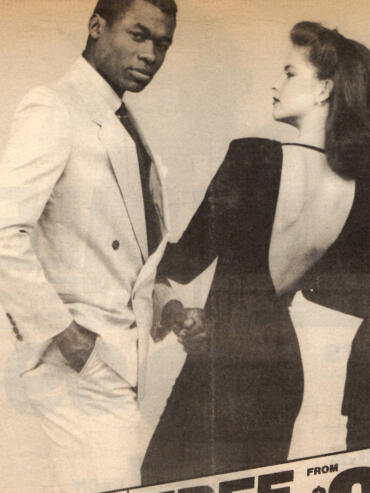Fashion photo featuring a man in a light-colored suit and woman in a backless black dress with voluminous hair.