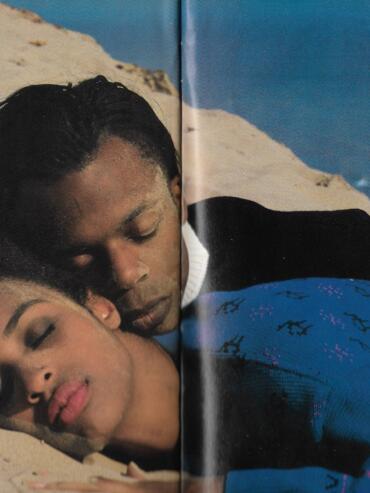 Couple embracing on a sandy beach, dressed in stylish, patterned clothing.