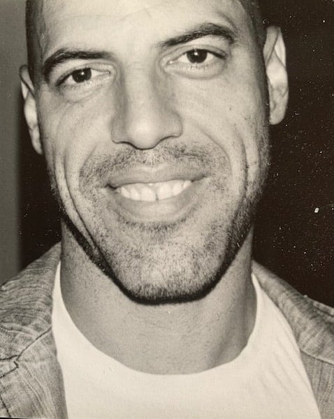 Close-up black and white portrait of a man with a friendly smile, casual style.