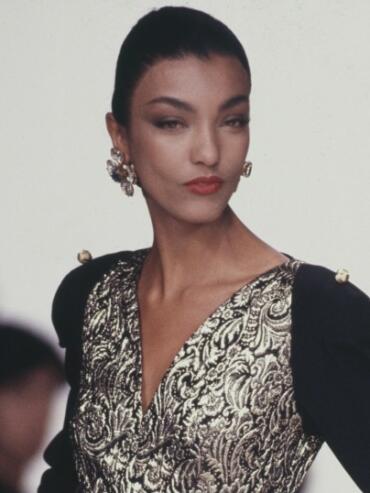 Elegant model in a black and gold patterned dress with statement earrings.
