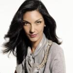 Elegant woman with dark, wavy hair wearing a silk scarf and a gray top.