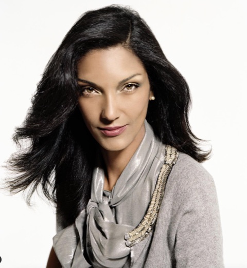 Elegant woman with dark, wavy hair wearing a silk scarf and a gray top.
