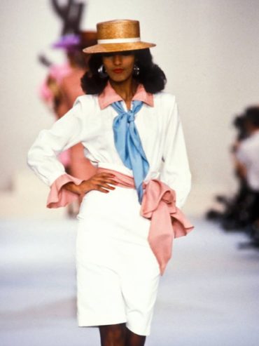 Model in a vintage-inspired outfit with a straw hat and pastel accents on a runway.