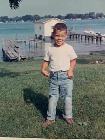 Young boy smiling in casual outfit near a lakeside dock.