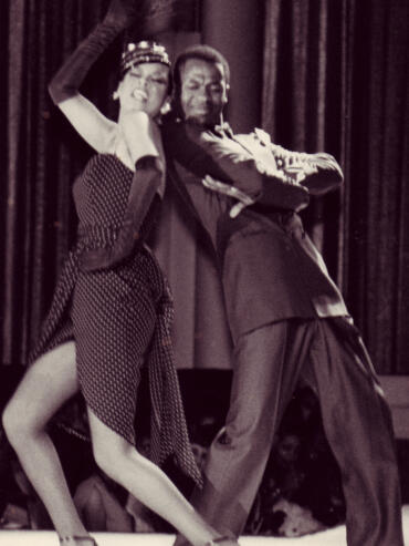 Black and white photo of a woman and man dancing closely; woman in polka-dot dress, man in suit.