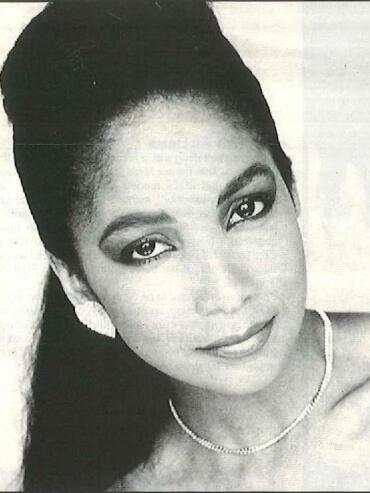 Black-and-white portrait of a woman with elegant makeup, jewelry, and a high updo hairstyle.