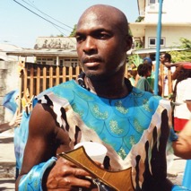 Man dressed in traditional attire with painted face and blue accessories.