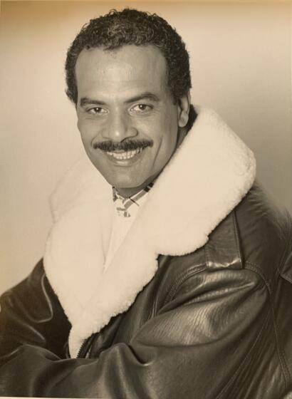 Portrait of a man in a leather jacket with a shearling collar, smiling warmly.