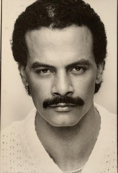 Black-and-white portrait of a man with a mustache, curly hair, and intense gaze, wearing a knit sweater.