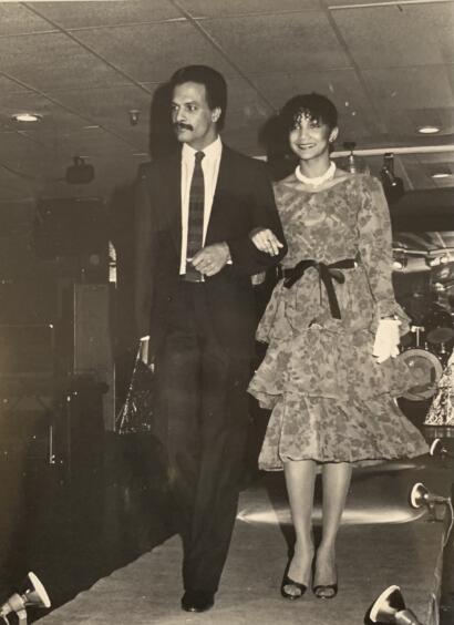 Black-and-white photo of a stylish man and woman walking arm-in-arm in formal attire.