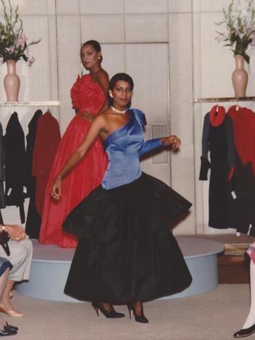 Two women modeling elegant evening wear on a fashion runway.