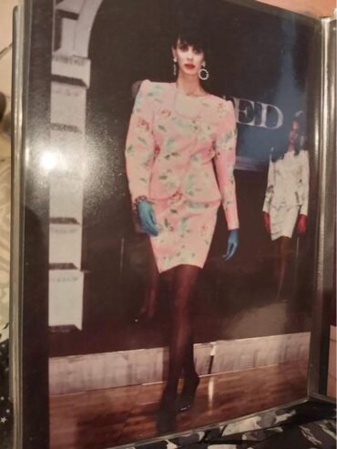 A woman in a pastel floral suit with dark tights and blue gloves, styled with statement earrings.