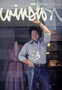 Person writing "Wimbledon" on a glass window, smiling and dressed casually.