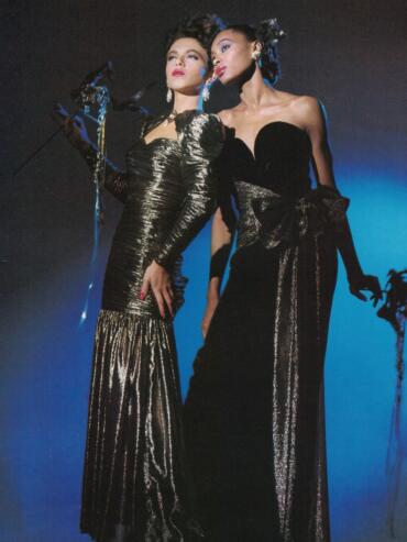 Two women in glamorous, black and gold evening dresses pose confidently, showcasing high fashion.