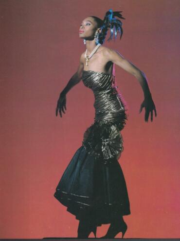 Model in a ruched gold silk strapless flamenco dress with black silk taffeta, accessorized with pearls and feathers.