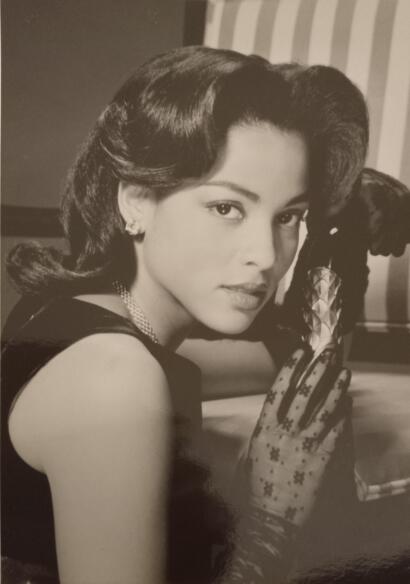 Elegant woman with vintage hairstyle, pearl necklace, and floral gloves in a classic black-and-white photo.